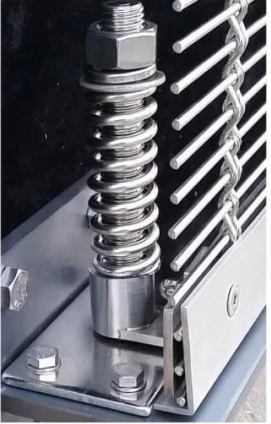 Close view of a spring and base support beside cable and rod mesh
